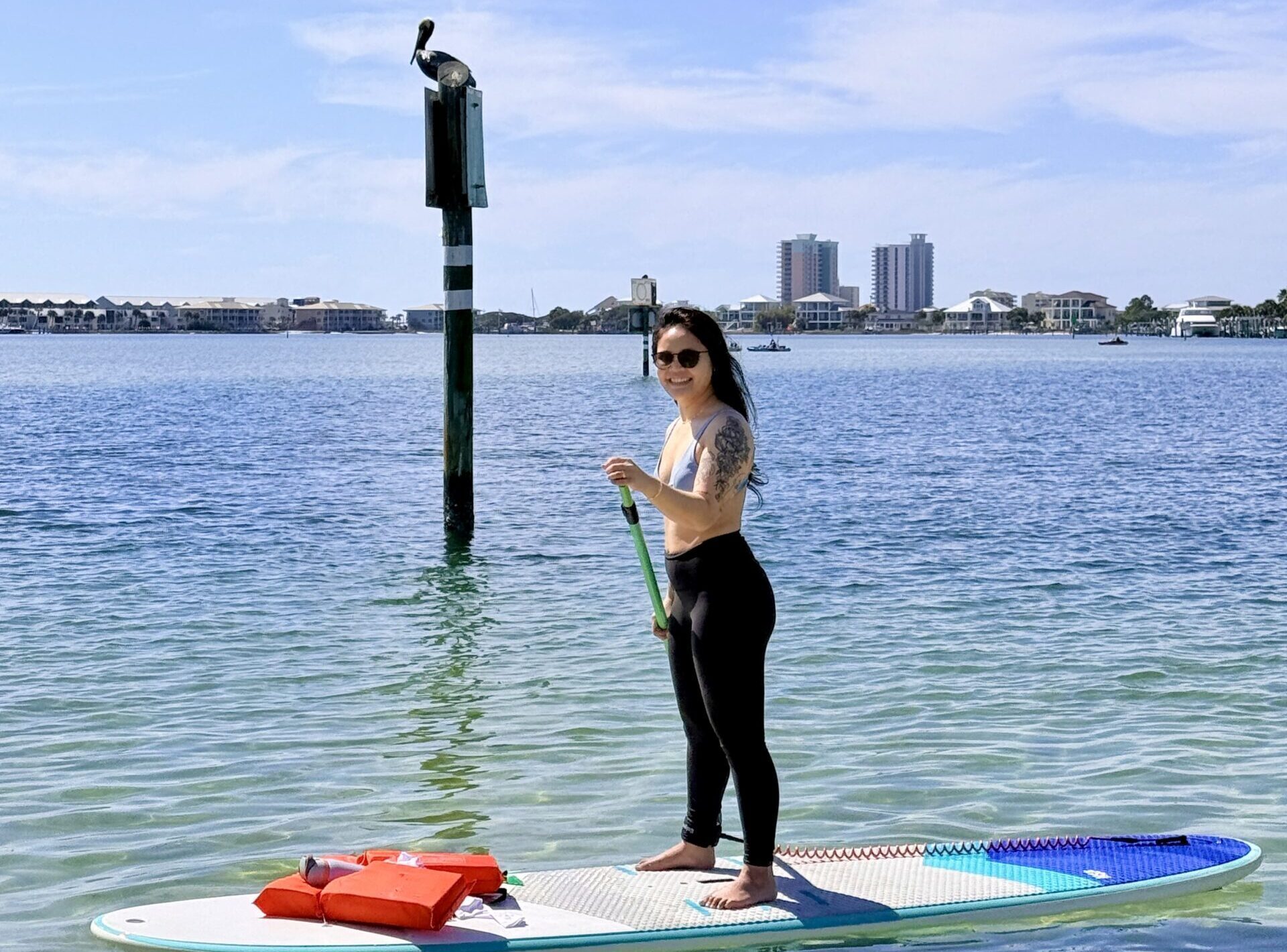 woman standing on a paddle board with pelican on a post in the background