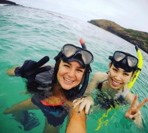 2 girls with snorkeling masks on their heads standing in water and holding up peace signs