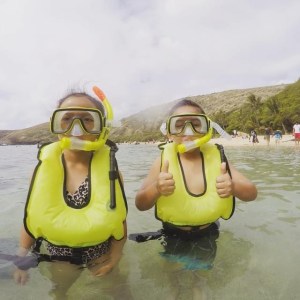 2 little kids standing in water while wearing life jackets and snorkel masks