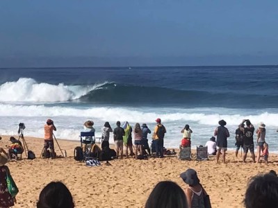 crowd of people standing on the beach watching large waves